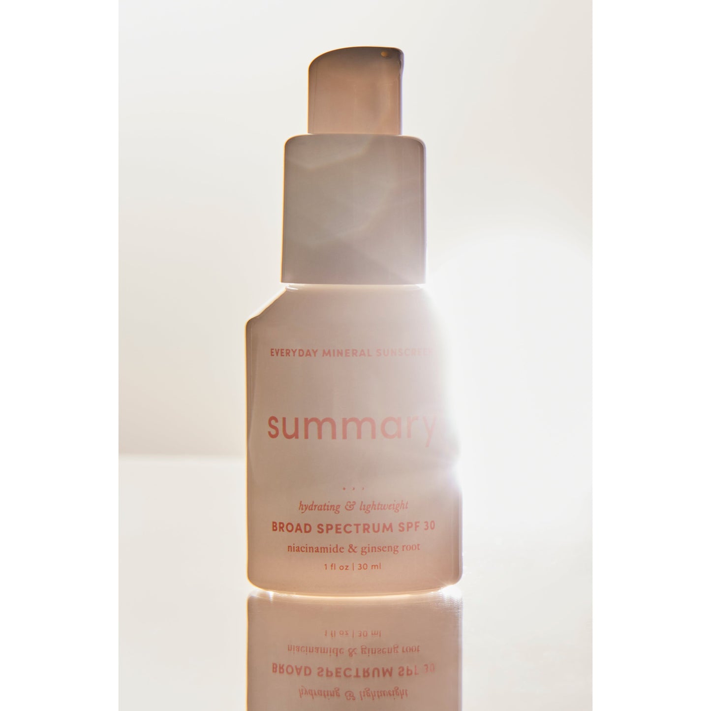 A bottle of Free People Movement's Summary SPF 30 mineral-based sunscreen backlit by sunlight, emphasizing its hydrating and lightweight formula.