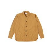 An oversized Travail Shirt in cumin by Universal Works with long sleeves, featuring a collar, two front pockets, and a stylish curved hem, displayed on a plain background.