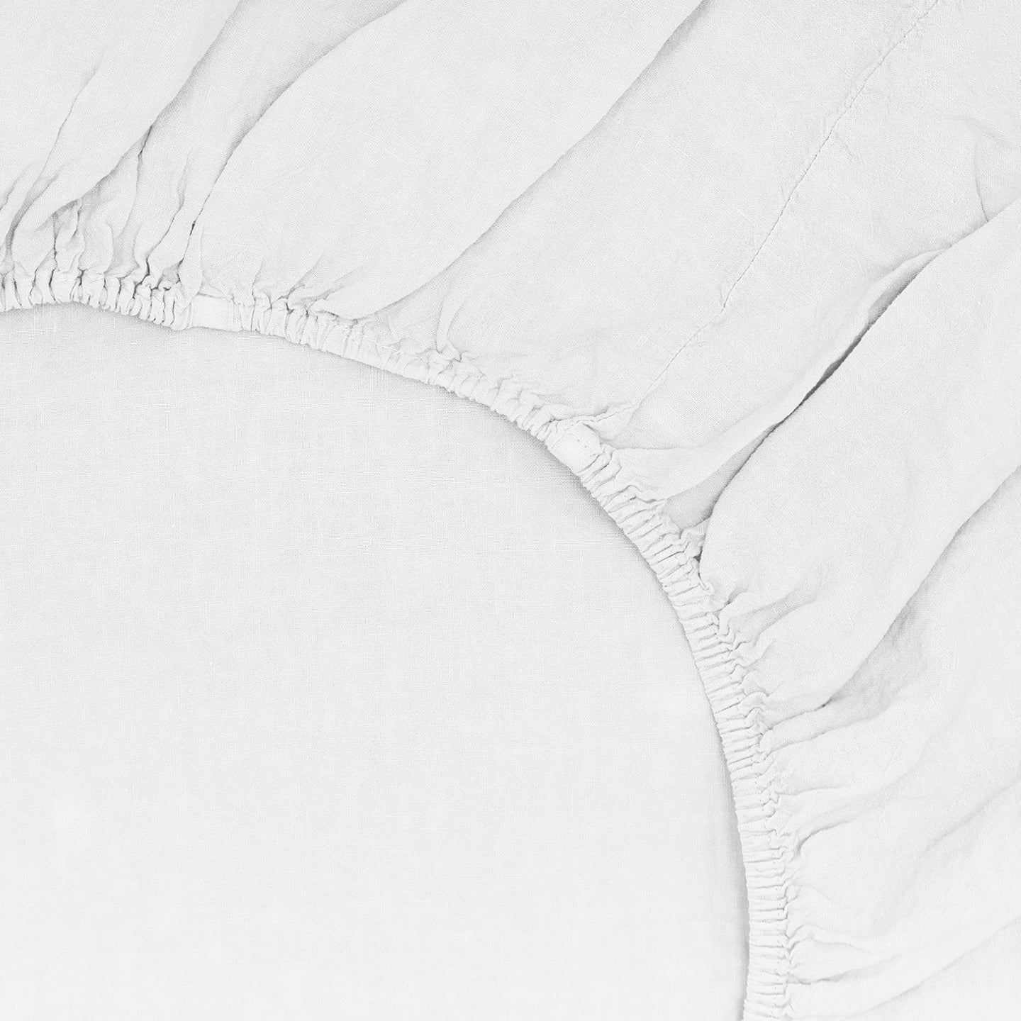 Close-up of the Simple Linen Fitted Sheet - Queen by Hawkins New York in stonewashed white, featuring gathered elastic edges and soft creases.
