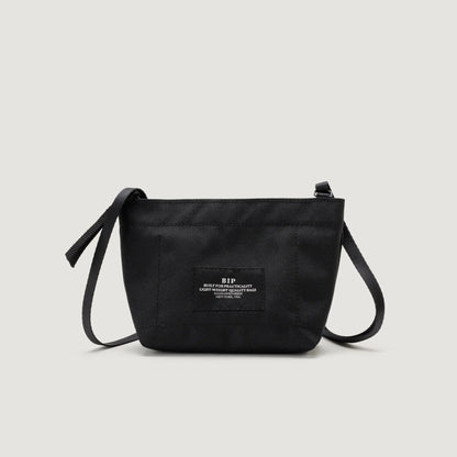 A black crossbody bag with a front Zipper Pouch Mini and adjustable strap, featuring a Bags in Progress label with text in the center.