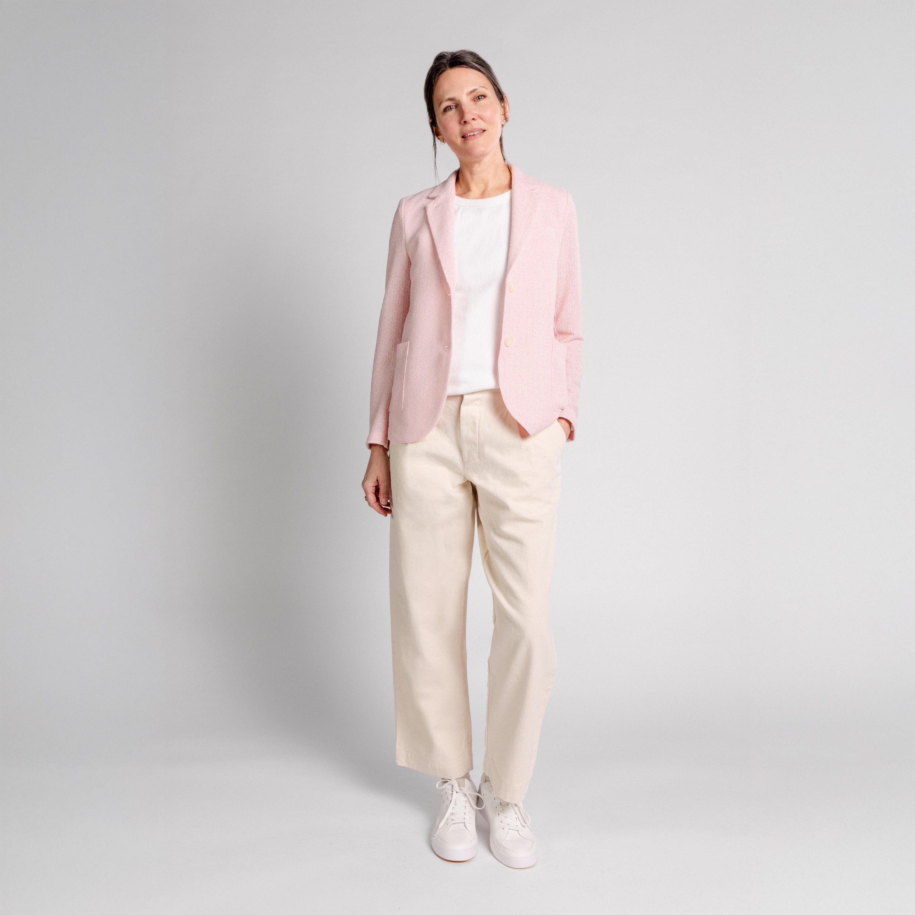 A woman stands against a plain background wearing the Harris Wharf W Stand Up Collar Bicolor Blazer Frize in pink, paired with a white t-shirt, beige trousers, and white sneakers.