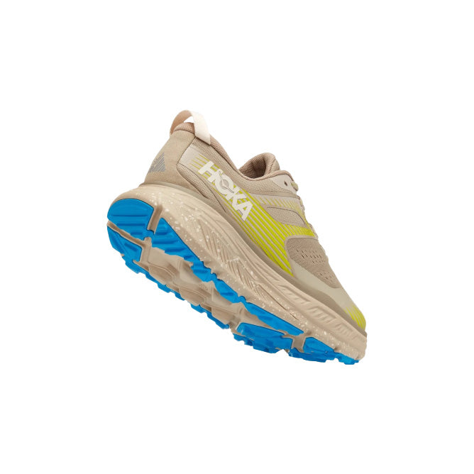 The Hoka M Stinson ATR 6 in DOTN features beige and yellow tones with a blue sole, shown from the back on a white background, delivering versatile comfort for every stride.