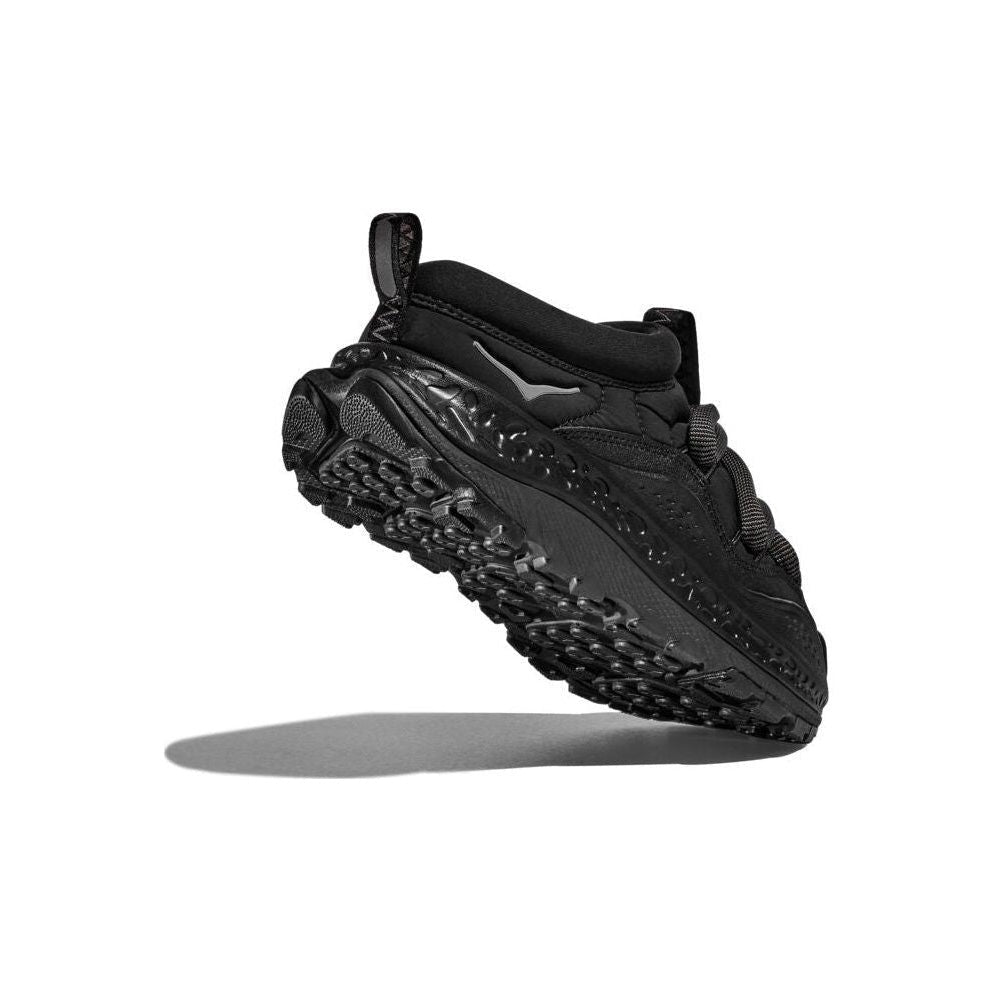 The Hoka U Ora Primo in black showcases its intricate tread pattern against a white background. Its insulated puff upper offers slip-on comfort, ideal for effortless wear.