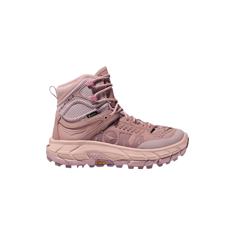 The Hoka U Tor Ultra Hi in Pale Mauve/Peach Whip is a hiking boot featuring mesh and synthetic panels, a thick rugged sole, and lace-up closure, shown from the side on a white background.