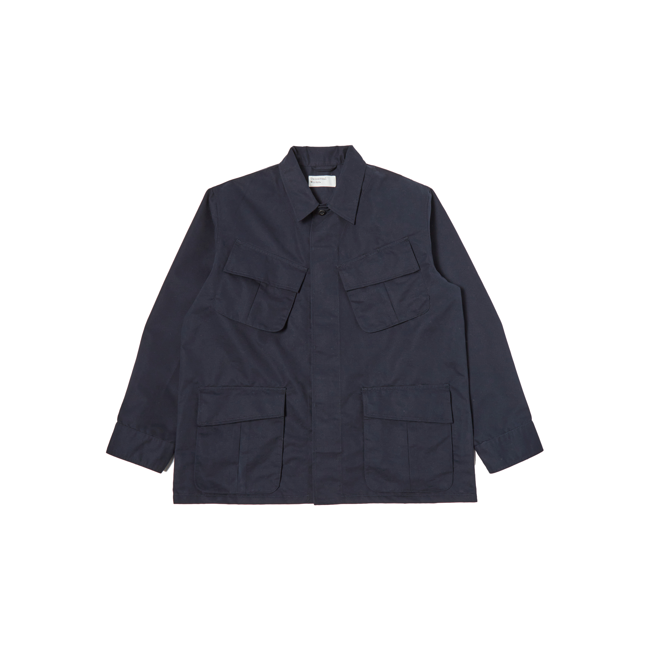 The Jungle Jacket by Universal Works is a dark blue utility jacket featuring a collared neck, long sleeves, and multiple flap pockets on the front. Crafted from recycled polyester for sustainability, this piece mirrors the iconic design of an Army Tropical Uniform Jacket.