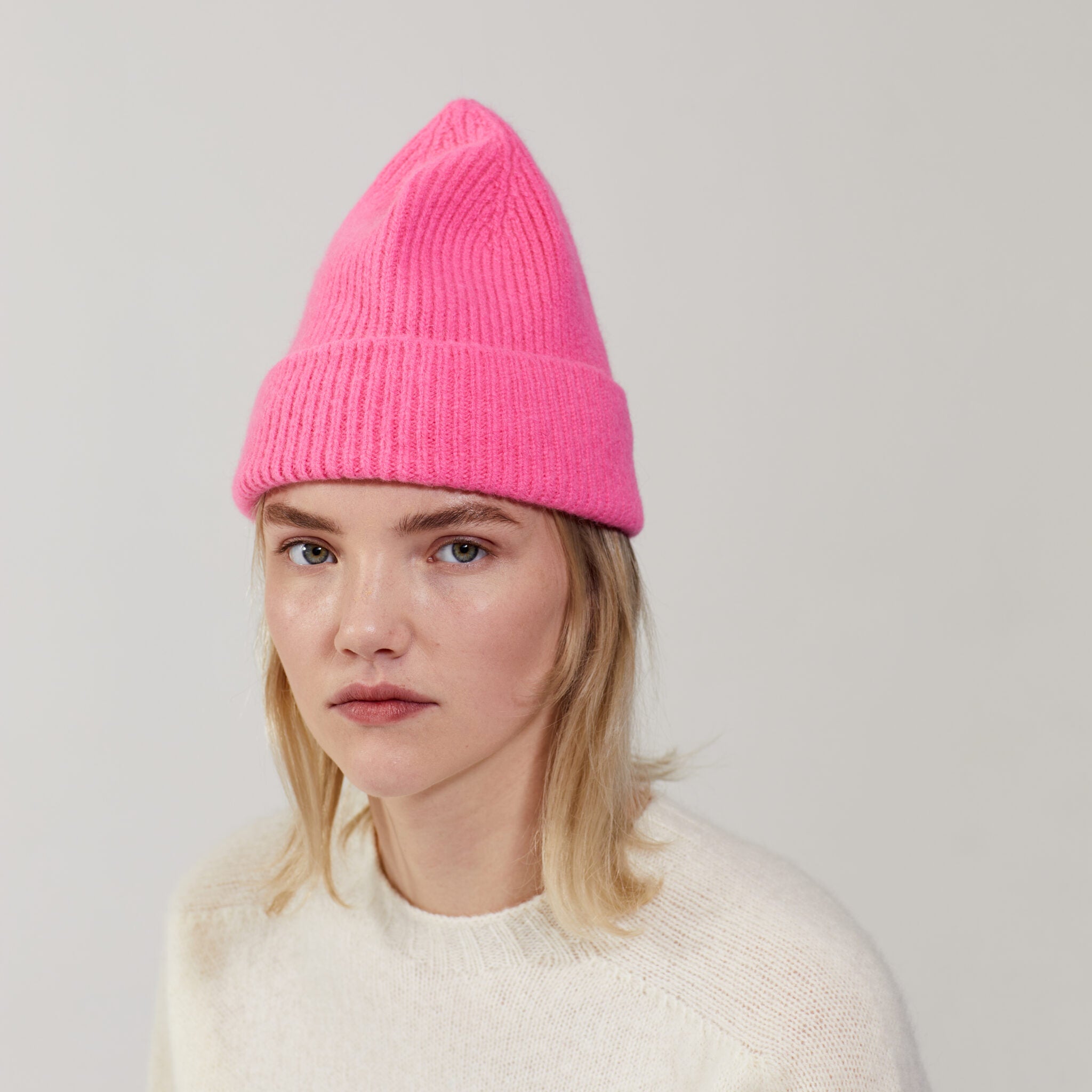 A person with light hair wears the Le Bonnet Beanie in Bubblegum and an off-white sweater, posing against a plain light background.