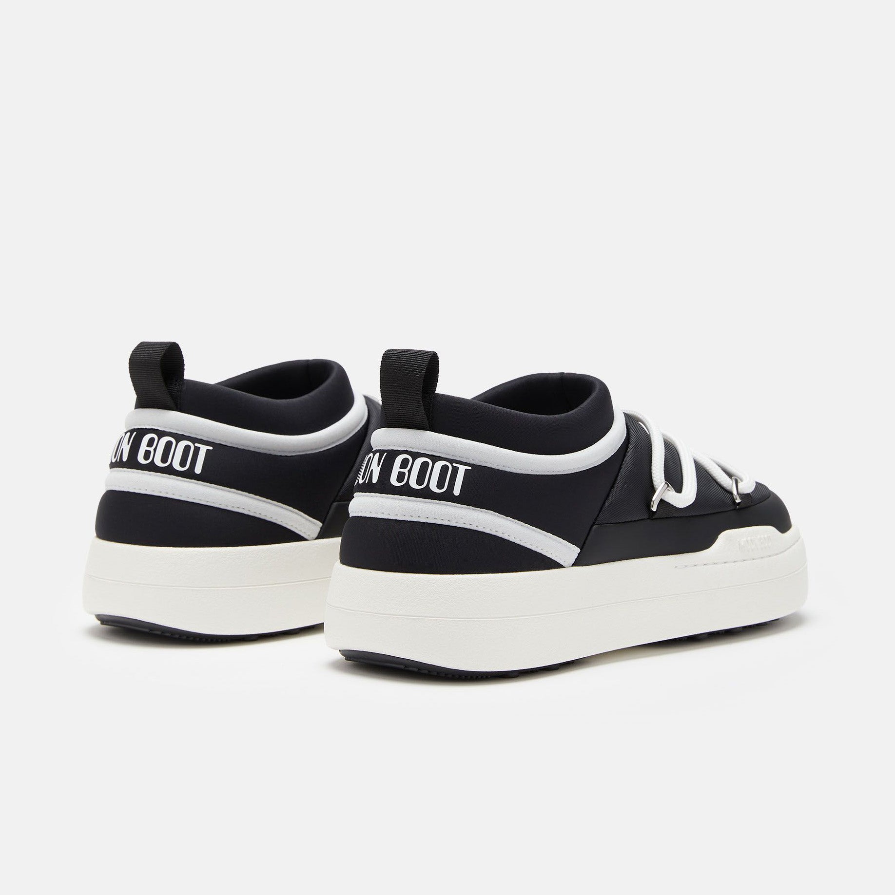The Park Icon sneakers by Moon Boot are black and white slip-ons with thick soles, "Moon Boot" text on the heel, a back loop, and ultra-flexible construction for ultimate comfort.