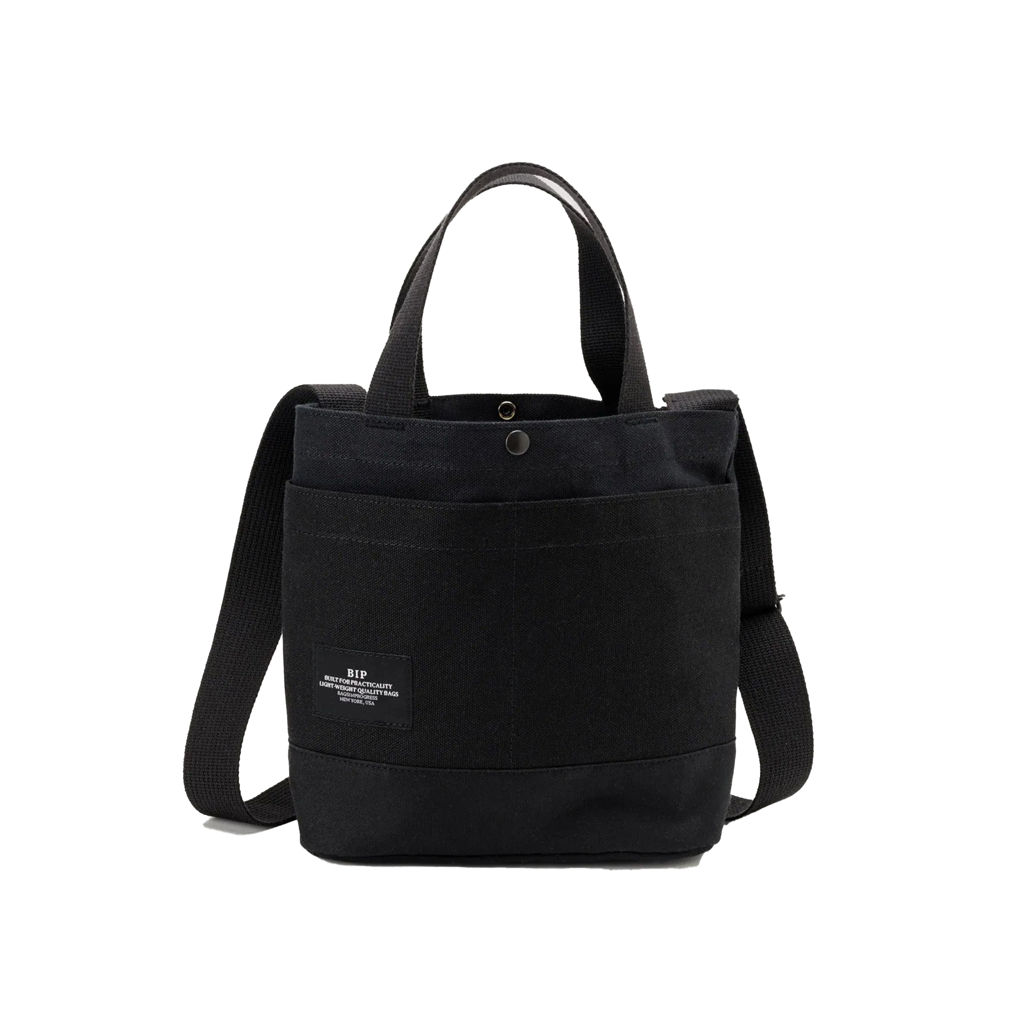 The New York Tote Small by Bags in Progress is a black cotton canvas tote bag featuring dual handles, an adjustable shoulder strap, and a front pocket with a small label on the front.