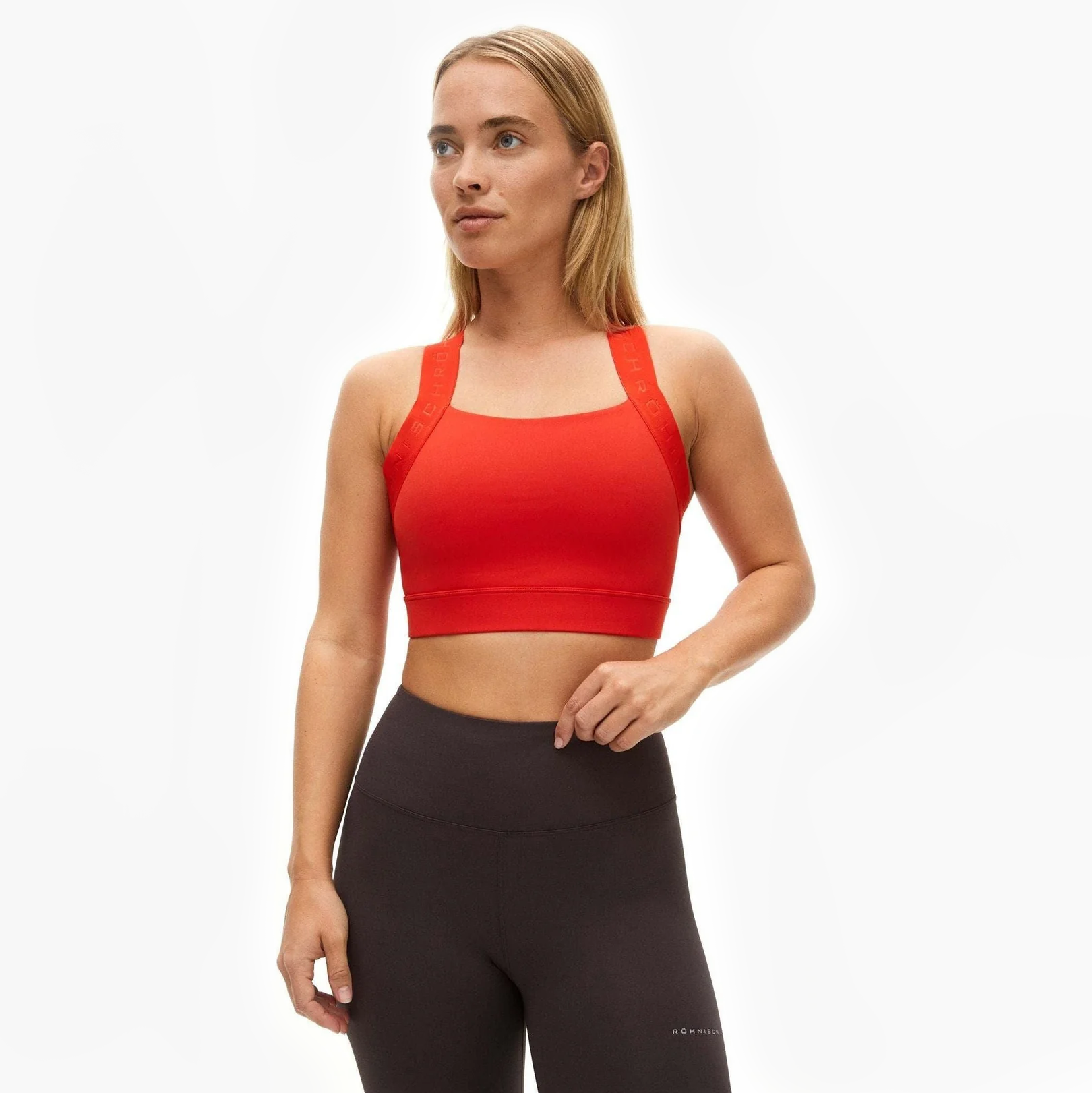 A woman wearing a red Rohnisch Kay Sports Bra and high-waisted black leggings stands against a plain white background.