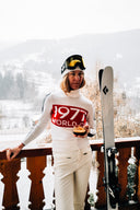 Layered Scandinavian outdoor clothing worn beside a cabin in a winter landscape