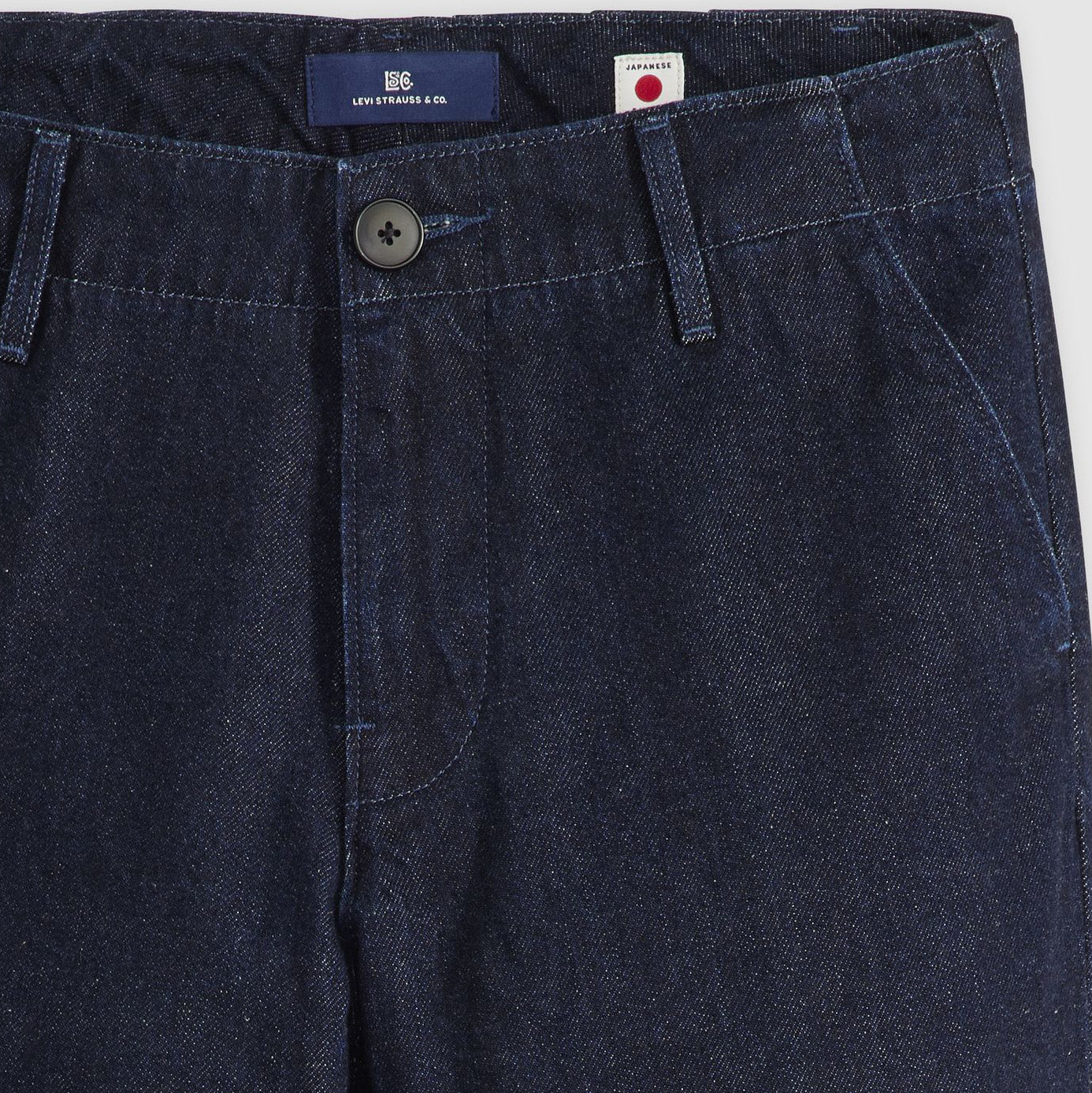 Close-up of the Levis Stem Flare Trouser in dark blue denim, featuring a black button, belt loops, front pockets, and a branded label on the waistband.