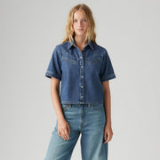 A woman faces forward in a Levi's Rinoa Camp Shirt—short-sleeved, button-up denim—paired with light blue jeans, capturing an Americana classic style against a plain light background.