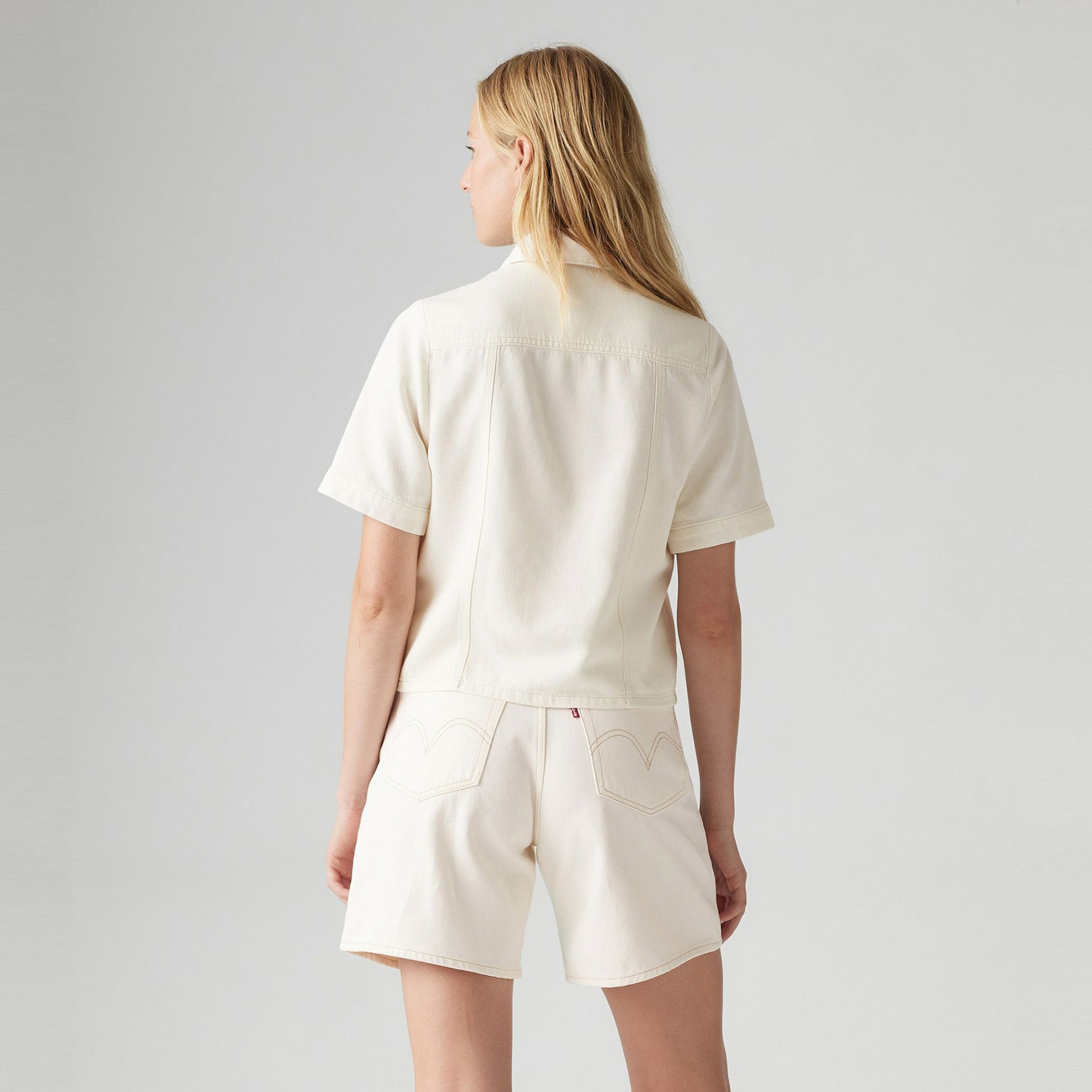 Woman with long blonde hair wearing a Levis Rinoa Camp Shirt and matching shorts, standing with her back to the camera against a plain background.
