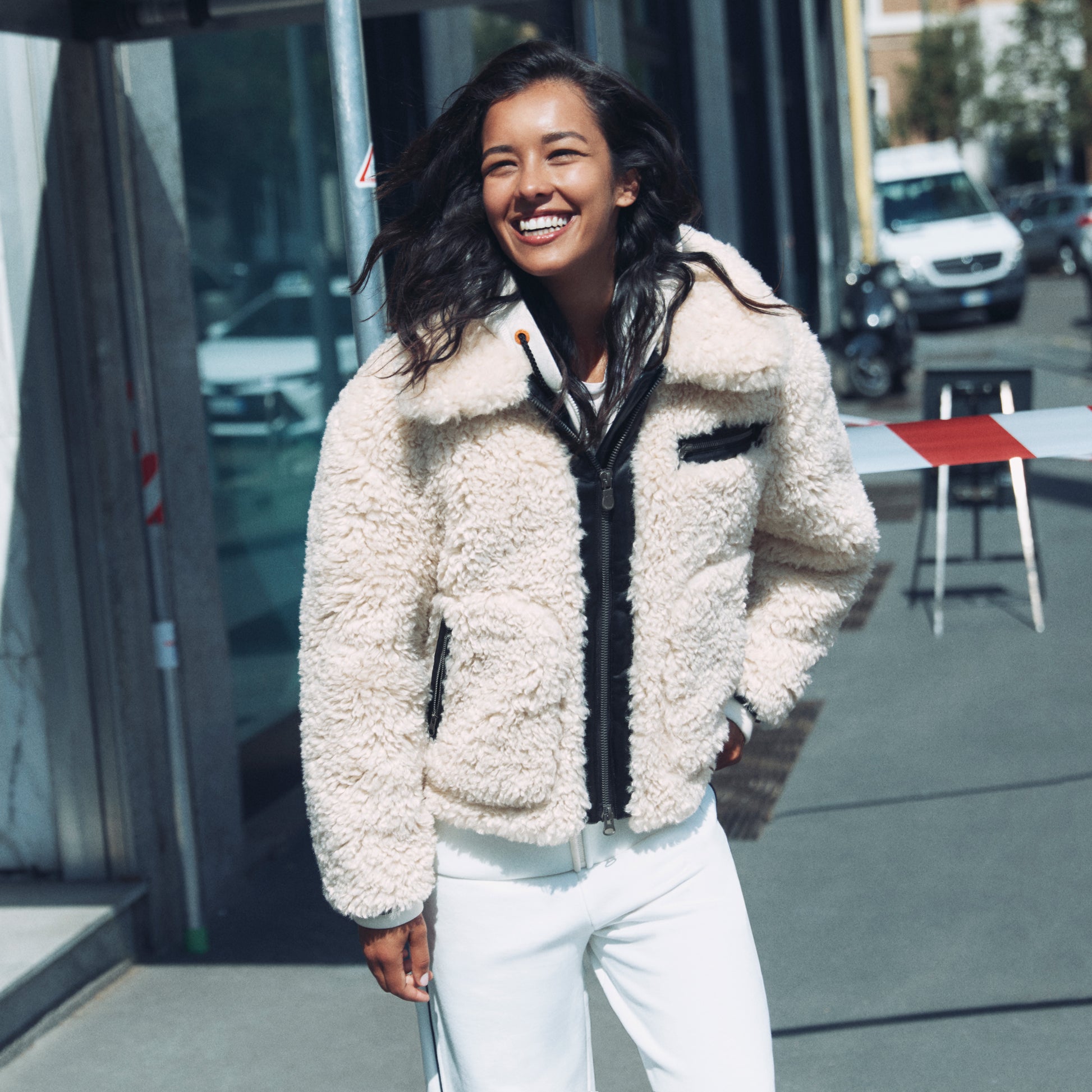 Woman wearing a beige sherpa jacket with black accents on a city street.