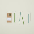 The Essential Glass Straws from Hawkins New York, including a cleaning brush and packaged in a cardboard box, are elegantly arranged on a light background.
