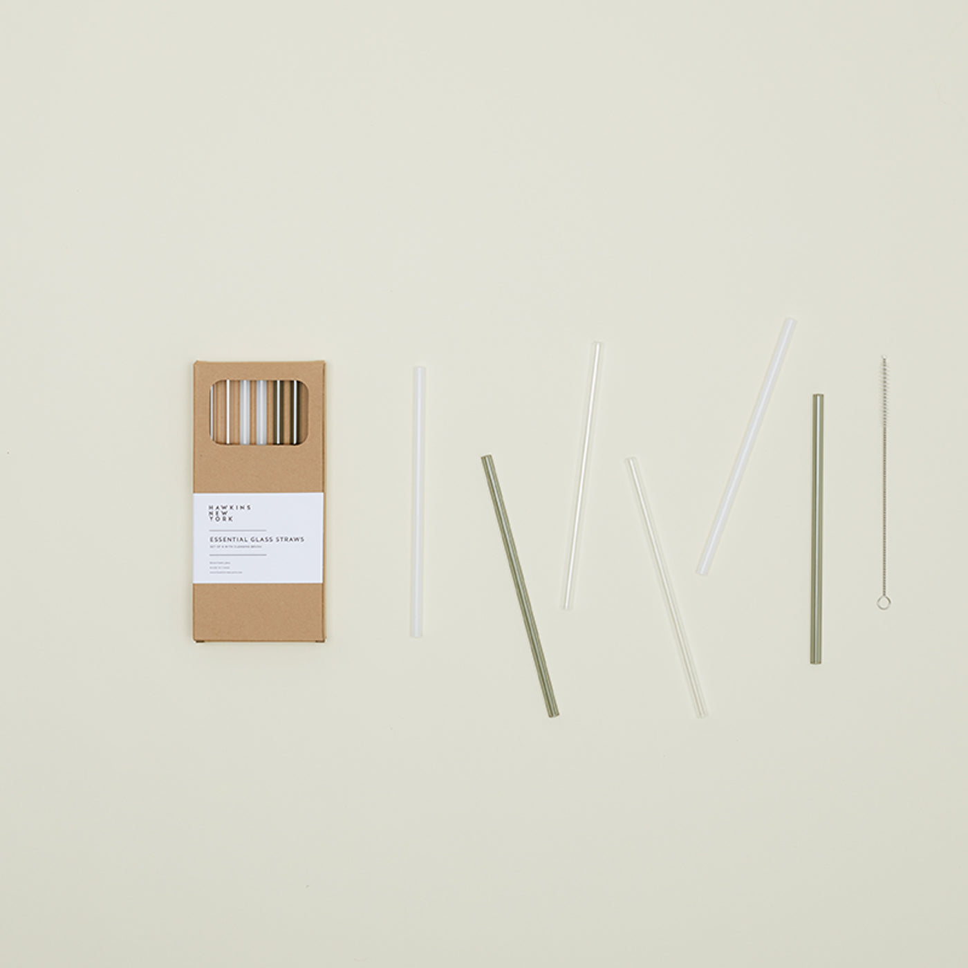 A box of Hawkins New York Essential Glass Straws - Set of 6 featuring clear and green straws with a cleaning brush is beautifully displayed on the left against a light background.