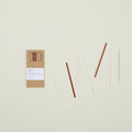 The Essential Glass Straws - Set of 6 by Hawkins New York, made from eco-friendly borosilicate glass and complete with a cleaning brush, are elegantly presented next to a brown cardboard box on a light background.
