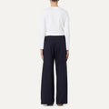 A person is seen from the back in a plain setting, wearing Labo Art's white cotton poplin long-sleeve shirt and black Panta Diana Pant, Clara wide-leg pull-on trousers.