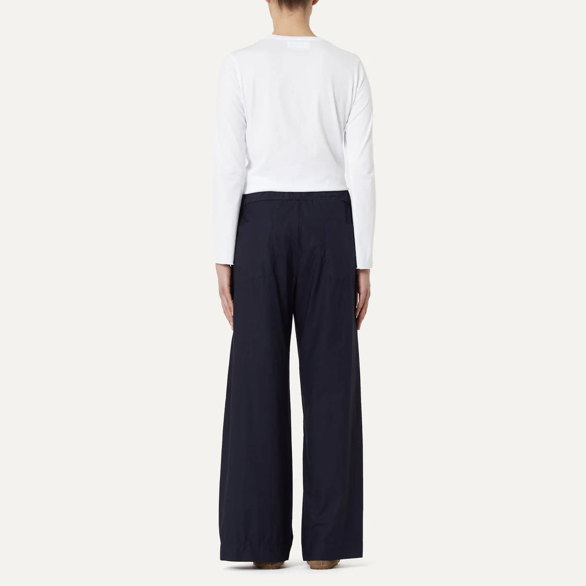 A person is seen from the back in a plain setting, wearing Labo Art's white cotton poplin long-sleeve shirt and black Panta Diana Pant, Clara wide-leg pull-on trousers.