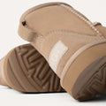 Close-up of two Ugg K Classic Mini II tan suede boots featuring visible stitching, cushioned outsoles, textured soles, and a logo on the side.