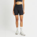 A person in a black sports bra and Rohnisch's Flattering High Waist Bike Shorts made from moisture-wicking fabric, complemented by white socks and gray sneakers, stands against a white background.