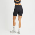 A person in a black sports bra and Rohnisch's Flattering High Waist Bike Shorts faces a white wall, wearing sneakers and white socks.