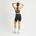 A person in black Rohnisch Flattering High Waist Bike Shorts and white socks, with arms raised, showcases the moisture-wicking fabric.