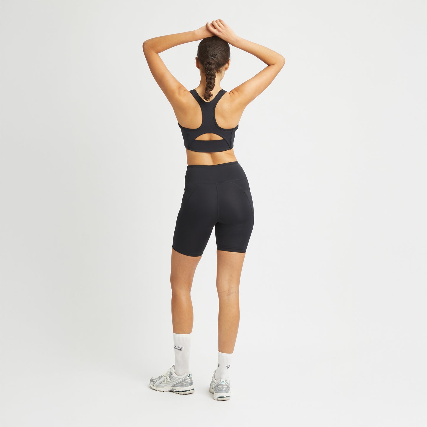 A person in black Rohnisch Flattering High Waist Bike Shorts and white socks, with arms raised, showcases the moisture-wicking fabric.