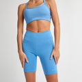 Wearing Rohnisch’s moisture-wicking Flattering High Waist Bike Shorts and a blue sports bra, a person stands against a white background.