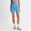 A person in a blue sports bra, Rohnisch Flattering High Waist Bike Shorts with an adjustable drawstring, white socks, and gray sneakers stands against a plain white background.