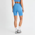 A person in a blue athletic outfit and silver sneakers faces away, wearing Rohnisch's Flattering High Waist Bike Shorts with an adjustable drawstring, paired with white socks featuring black text.