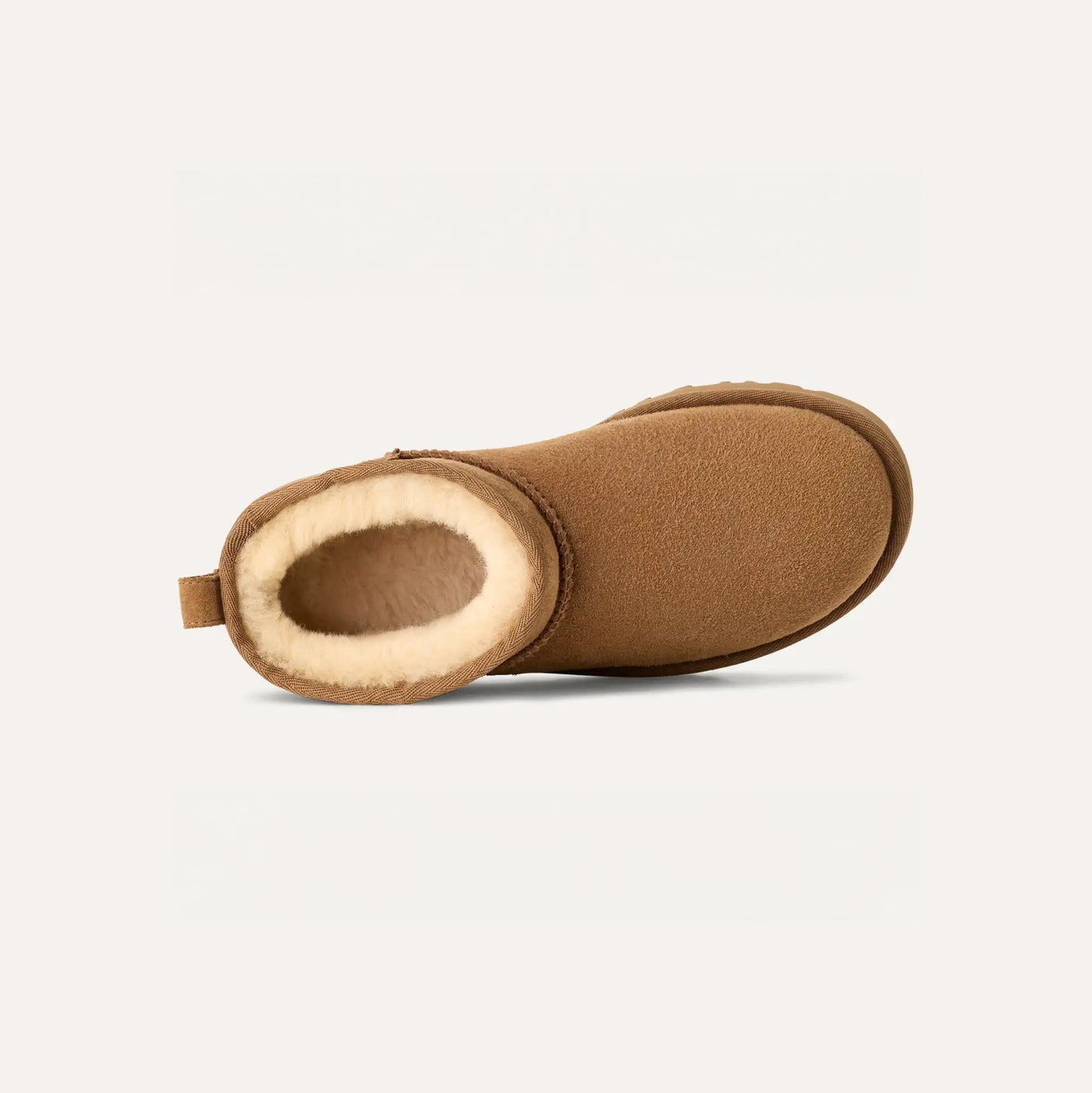 The W Classic Ultra Mini by Ugg is a brown slipper boot with UGG sheepskin, a shearling lining, an ultra-light sole, and a back loop. Its side profile is showcased against a plain background.