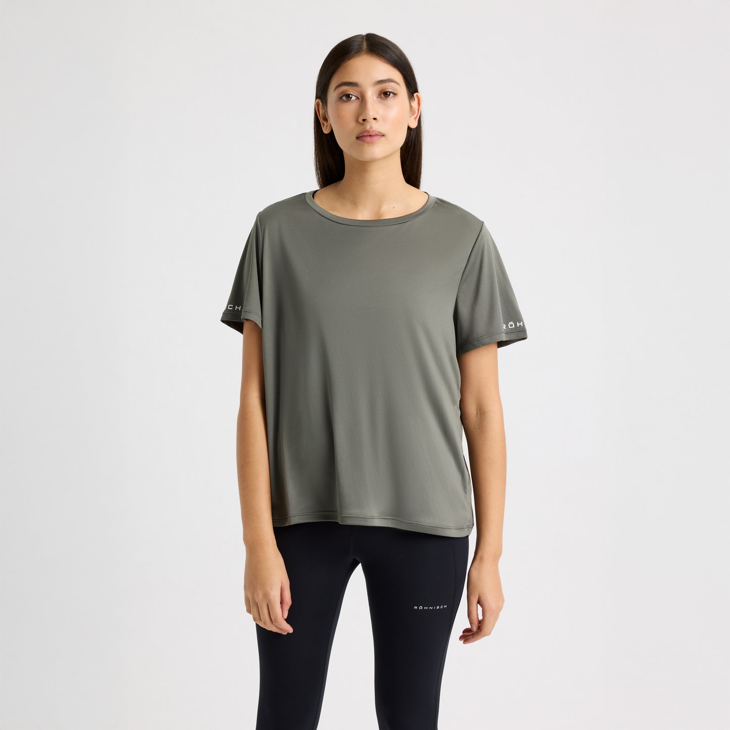 A person wearing a green Rohnisch Team Logo Short Sleeve T-shirt and black leggings stands against a plain white background.