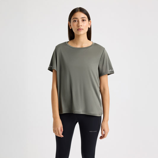 A person wearing a green Rohnisch Team Logo Short Sleeve T-shirt and black leggings stands against a plain white background.