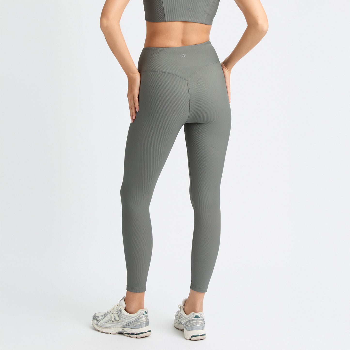 A person in Rohnisch Ribbed Regular High Waist Tights and a matching sports top stands with hands on hips, facing away. They wear sneakers, and the activewear is made from recycled polyester for an eco-friendly touch.