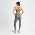 A woman in a matching gray workout outfit and sneakers, featuring Rohnisch Ribbed Regular High Waist Tights made from recycled polyester, stands with her hands on her hips against a plain white background.