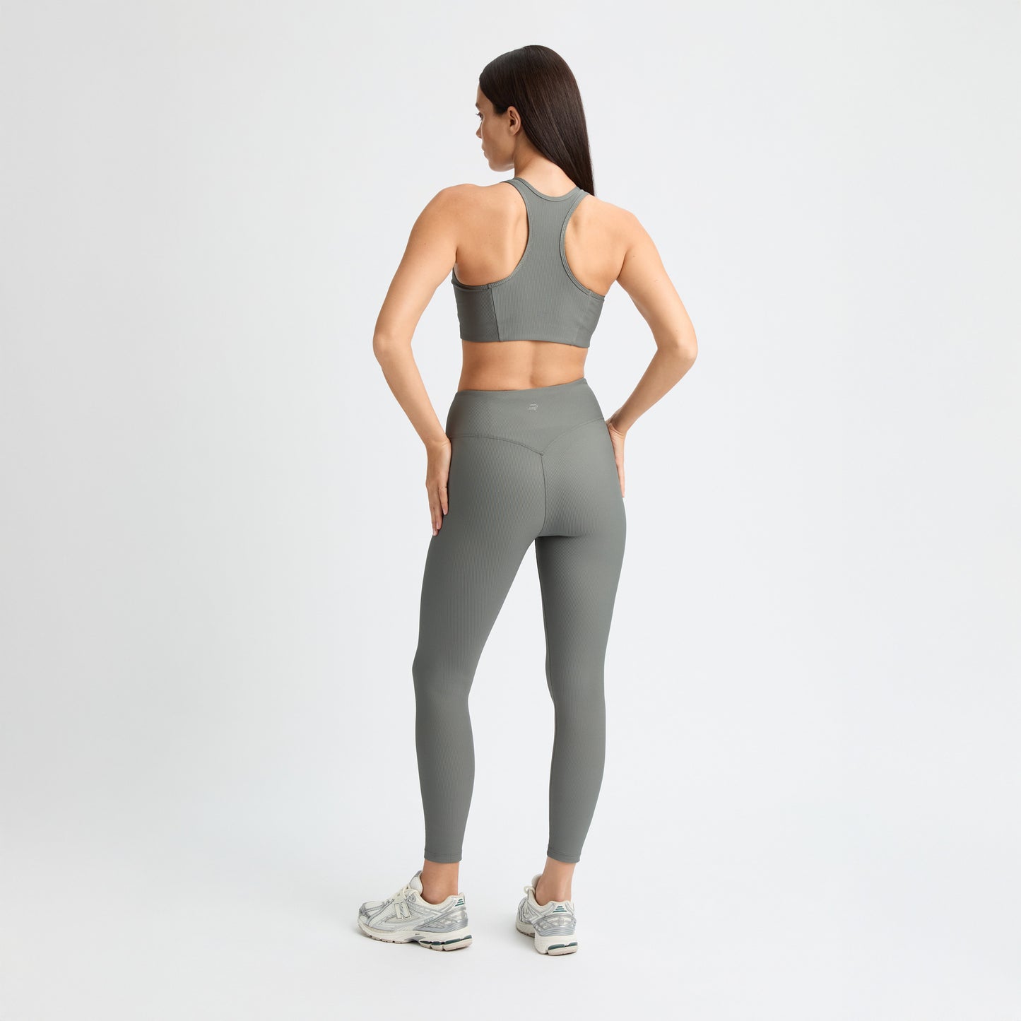 A woman in a matching gray workout outfit and sneakers, featuring Rohnisch Ribbed Regular High Waist Tights made from recycled polyester, stands with her hands on her hips against a plain white background.