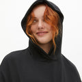 A red-haired person smiles warmly in the sleek Soft Jersey Hoodie by Rohnisch, made from recycled polyester, against a plain white backdrop.