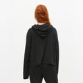 A person with long red hair is shown from the back, wearing a black Soft Jersey Hoodie and pants made from recycled polyester by Rohnisch against a plain white background.
