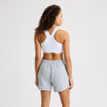 A person with curly hair in a white sports bra and gray Soft Sweatshort from Rohnisch faces away from the camera against a plain background.