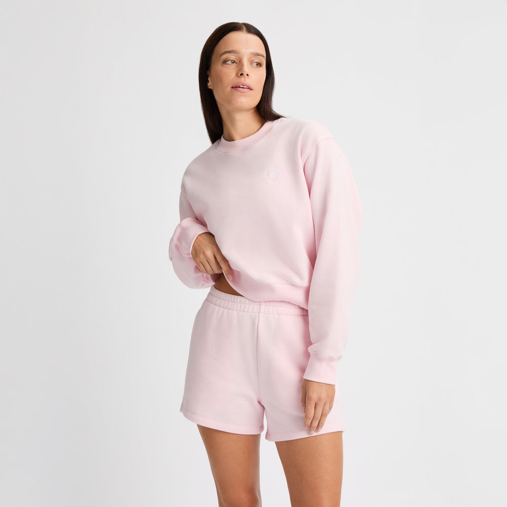 A person wearing a light pink terry fabric sweatshirt and Rohnisch's Soft Sweatshorts stands against a plain background, looking to the side.