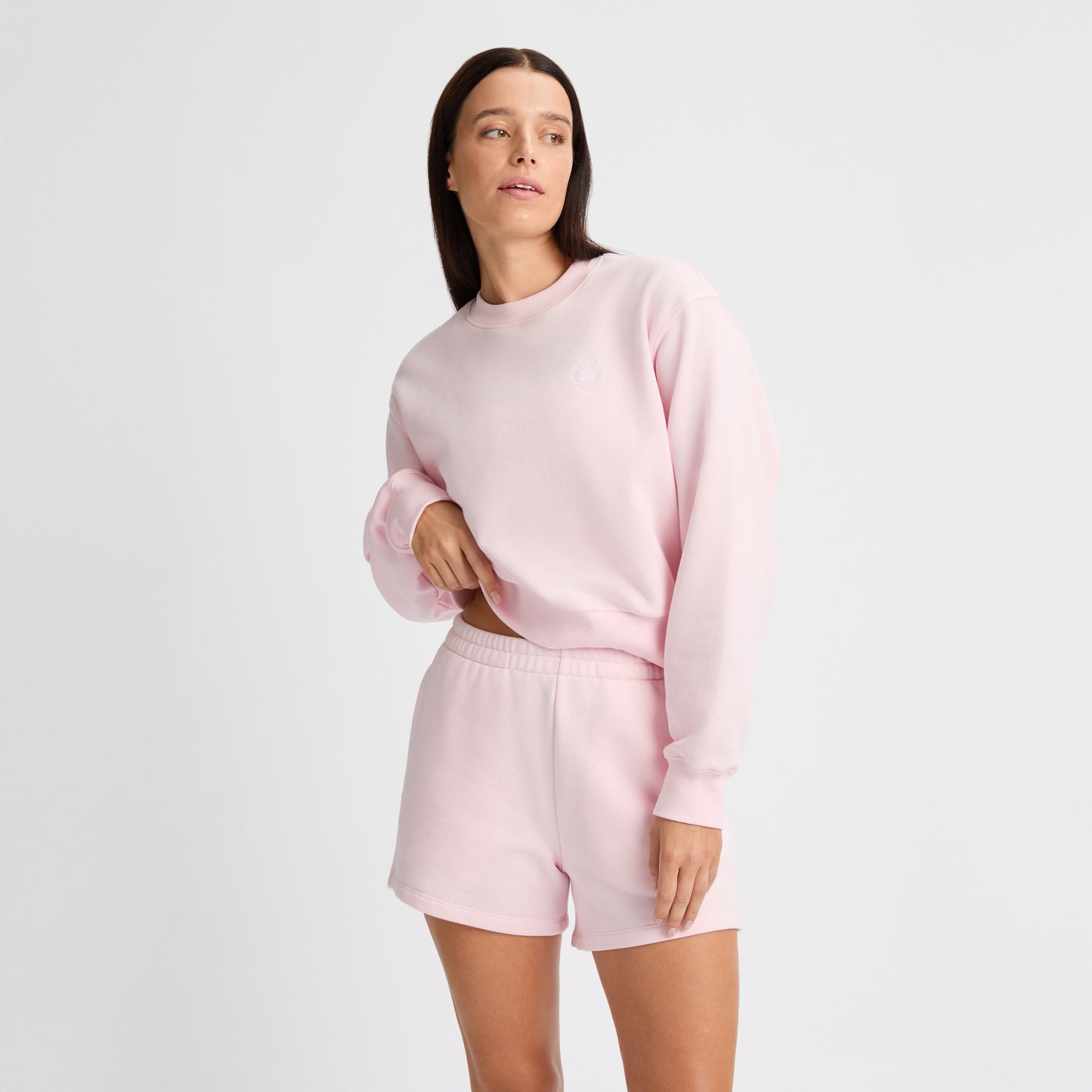 A person wearing a light pink terry fabric sweatshirt and Rohnisch's Soft Sweatshorts stands against a plain background, looking to the side.
