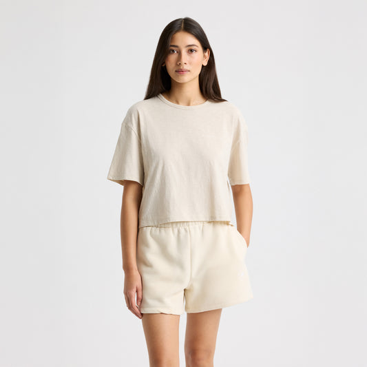 Against a plain backdrop, someone dons Rohnisch's beige Slub Cropped Tee and matching shorts. The tee's boxy fit accentuates the casual elegance of in-conversion cotton, crafting a relaxed yet stylish look.