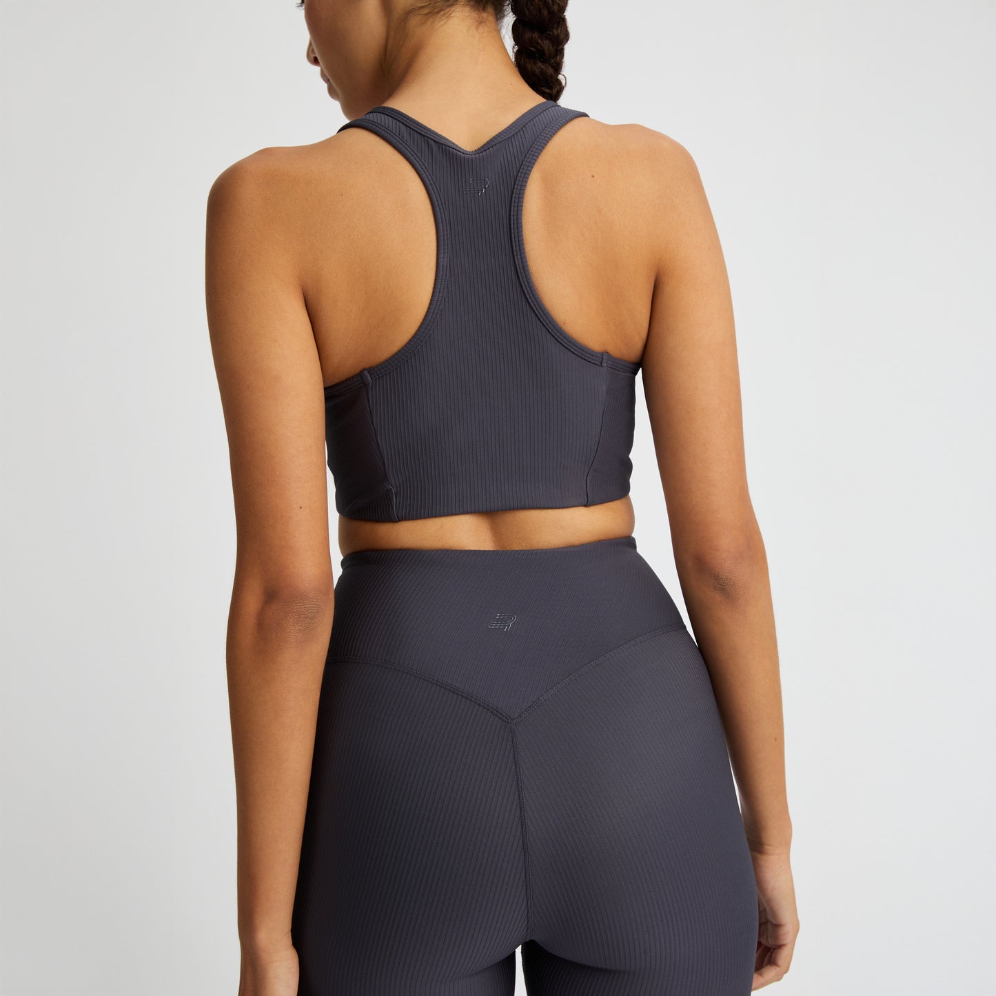 A person wearing a medium-support Rohnisch Ribbed Sportsbra and leggings, made from recycled polyester, stands against a plain background.