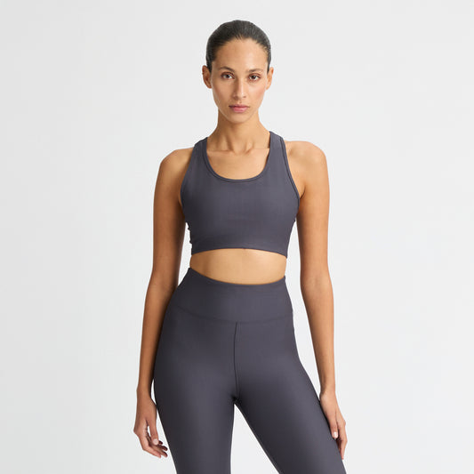 A person confidently poses against a plain white background wearing a Ribbed Sportsbra by Rohnisch, part of their dark athletic outfit.