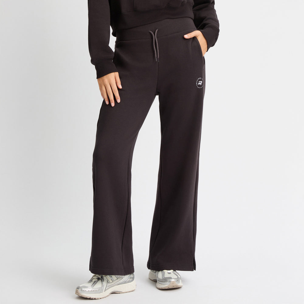 A person is wearing Rohnisch's Soft Sweat Wide Pants in black with a matching recycled sweatshirt fabric hoodie, white sneakers, and has one hand on their hip.