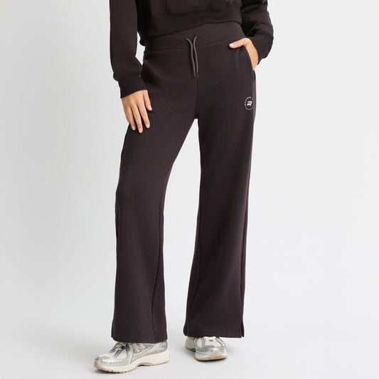A person is wearing Rohnisch's Soft Sweat Wide Pants in black with a matching recycled sweatshirt fabric hoodie, white sneakers, and has one hand on their hip.