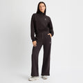 A woman in a black zip-up sweatshirt made from recycled fabric and Rohnisch's Soft Sweat Wide Pants stands with one hand in her pocket against a plain white background.