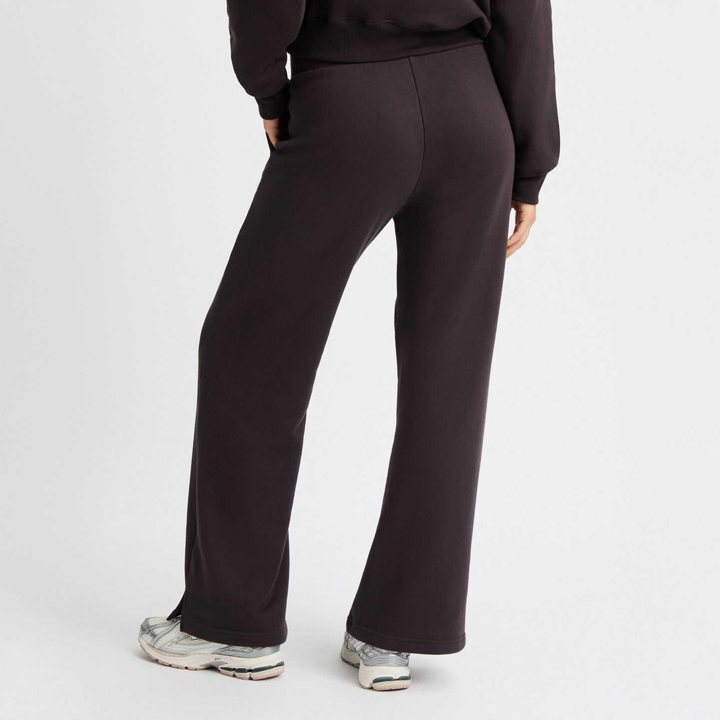 A person faces away, wearing Rohnisch Soft Sweat Wide Pants in black with a matching top made of recycled sweatshirt fabric. The outfit pairs perfectly with white sneakers against a plain white background.
