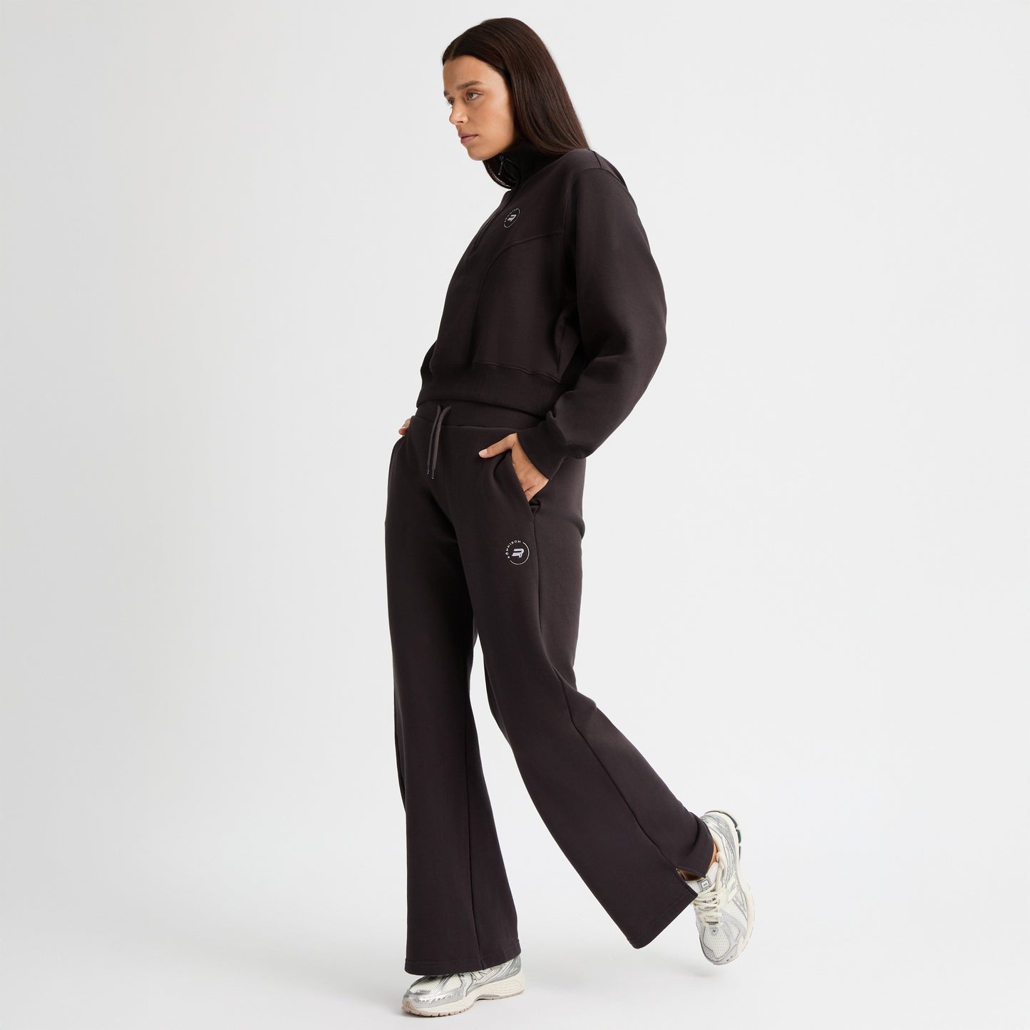 Someone wearing Rohnisch's Soft Sweat Wide Pants in black and silver sneakers stands in profile with hands in pockets against a plain white background.